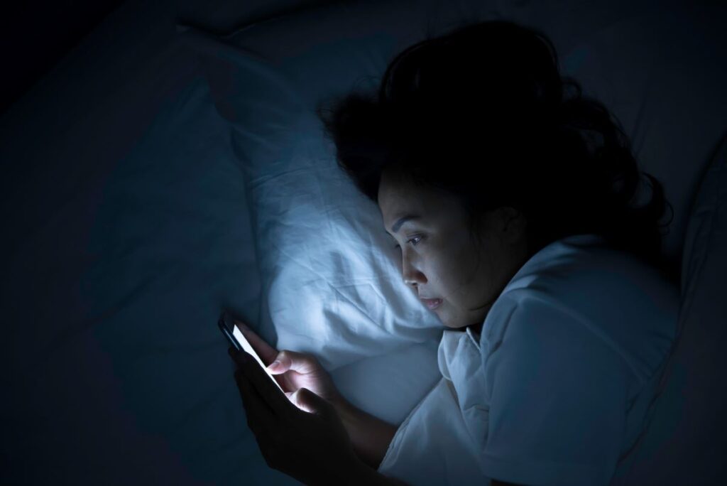 A woman looking at a cell phone in bed.